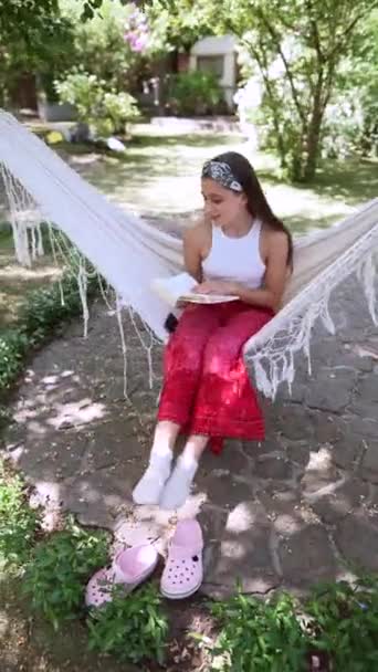 The beautiful hippie girl is swinging in a hammock and flipping through a book. High quality 4k footage - Filmati, video