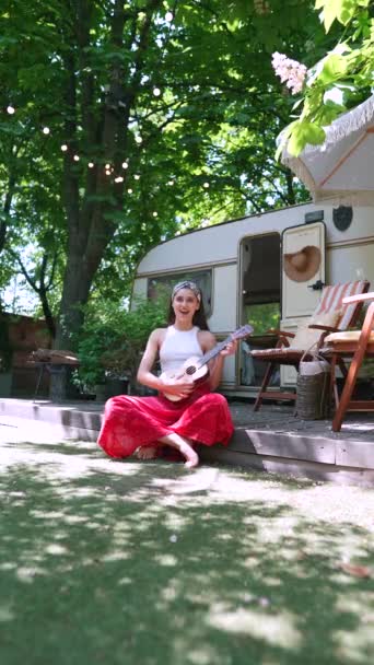  beautiful hippie girl is singing a song and playing the guitar near the trailer. High quality 4k footage - Metraje, vídeo