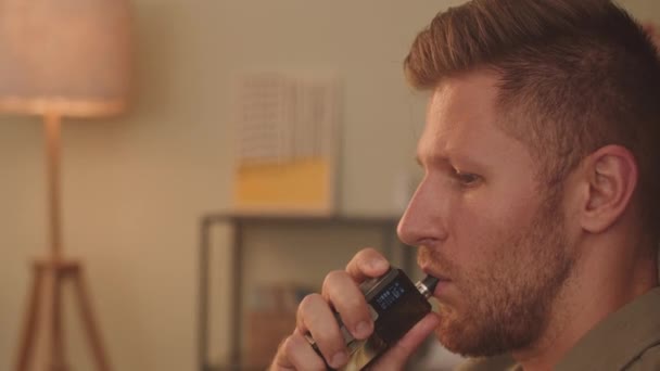 Side view close up of young Caucasian man vaping while reading at home - Video