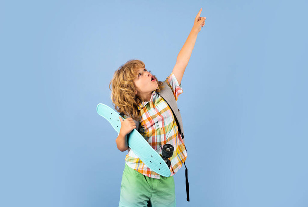 Studio portrait of stylish cute young child boy with skateboard isolated against blue background. Kid skater. Childhood and happy time. Cute child with skateboard and backpack - Valokuva, kuva