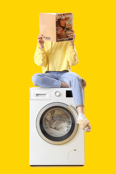 Mulher sentada na máquina de lavar roupa e revista de leitura contra fundo amarelo - Foto, Imagem