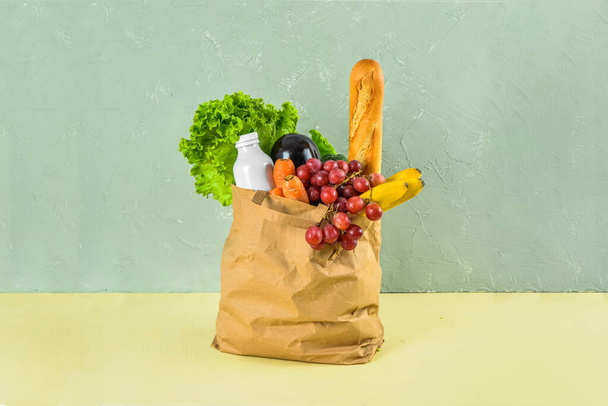 Papier torba pełna świeżego jedzenia na żółtym stole w pobliżu zielonej ściany grunge. Koncepcja dostaw żywności - Zdjęcie, obraz