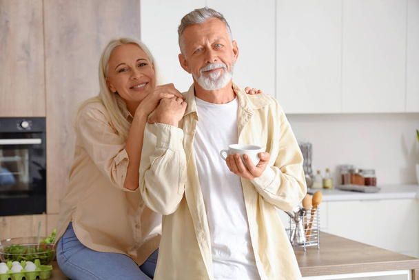 Mature homme avec tasse de café et sa femme dans la cuisine - Photo, image