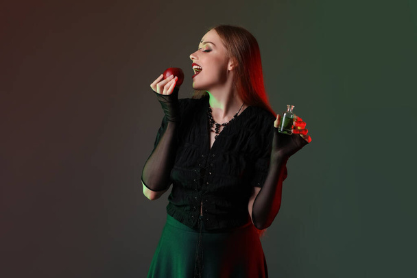 Krásná mladá čarodějnice s jablkem a lektvarem na tmavém pozadí - Fotografie, Obrázek