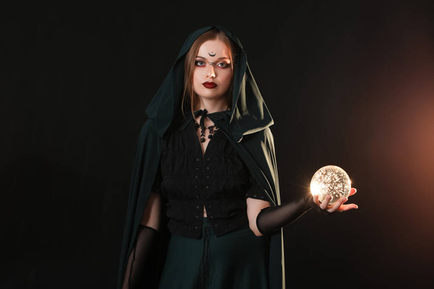 Bruxa jovem bonita com bola de cristal no fundo escuro - Foto, Imagem