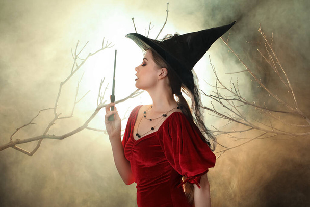 Hermosa bruja joven con varita mágica sobre fondo oscuro - Foto, imagen