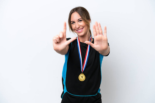 Mujer joven caucásica con medallas aisladas sobre fondo blanco contando siete con dedos - Foto, Imagen