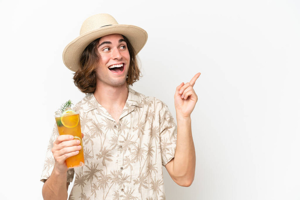 Joven hombre guapo sosteniendo un cóctel aislado sobre fondo blanco con la intención de realizar la solución mientras levanta un dedo - Foto, Imagen