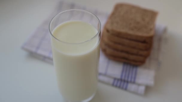 In Zeitlupe Milch in Glas auf dem Küchentisch gießen. Glas frische Milch mit Sauerteigbrot zum Frühstück - Filmmaterial, Video