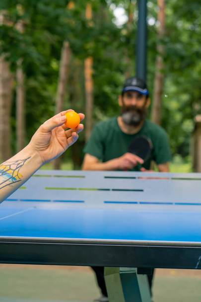 Gros plan d'une balle de ping-pong servie sur le fond d'un homme plus âgé à la barbe grise qui se prépare à frapper la balle - Photo, image