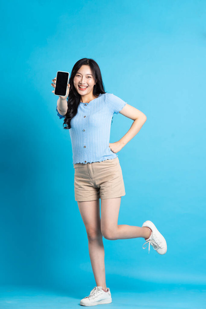 πλήρη εικόνα του σώματος του όμορφου κοριτσιού από την Ασία ποζάροντας σε μπλε φόντο - Φωτογραφία, εικόνα