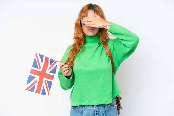 Молода жінка, що тримає прапор Великої Британії, ізольована на білому тлі, закриваючи очі руками. Не хочу нічого бачити. - Фото, зображення
