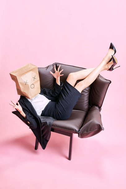 Stress at work. Woman sitting with paper bag on head and working on laptop against pink studio background. Concept of business, working routine, deadlines, freelance, office, ad - Photo, image