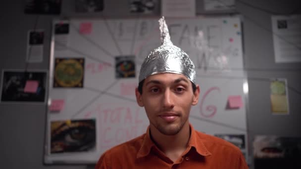 Strange stupid young man conspiracy theorist in protective foil cap with bitcoin coins in his eyes looking at camera. Conspiracy theory concept. Fake and alternative facts. Cryptocurrency and mind - Footage, Video