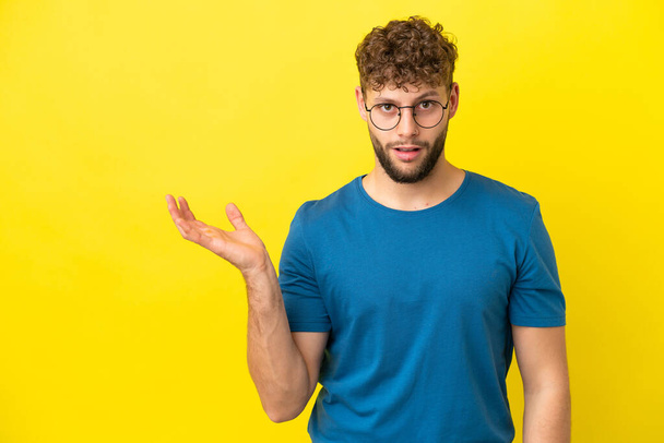 Jonge knappe blanke man geïsoleerd op gele achtergrond maken twijfels gebaar - Foto, afbeelding