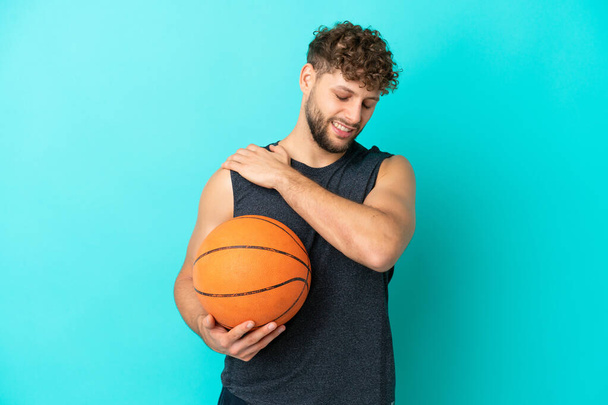 努力をしたことのための肩の痛みに苦しんでいる青い背景で隔離されたバスケットボールをするハンサムな若い男 - 写真・画像