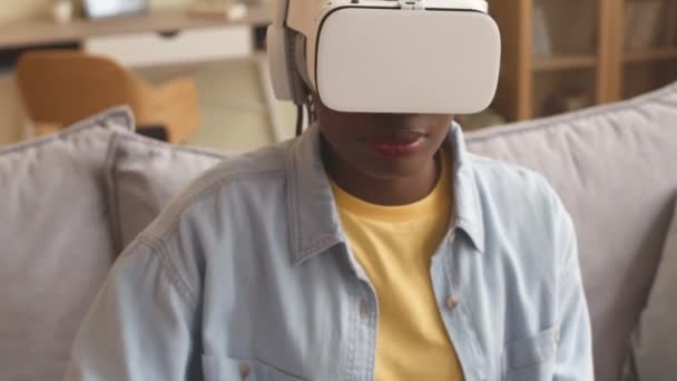 Medium closeup of concentrated African American girl in vr headset playing vr games at home using controller - Materiał filmowy, wideo