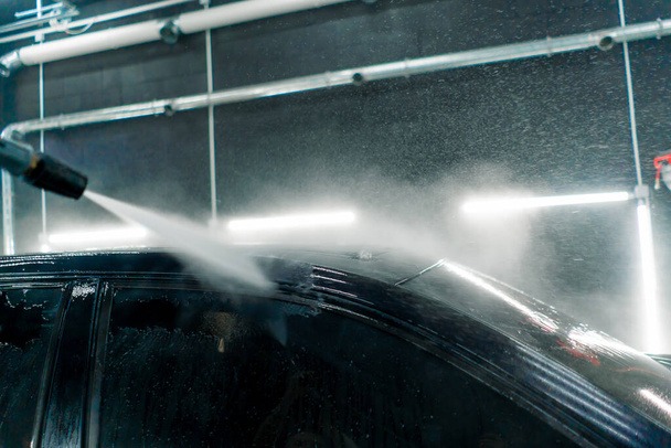 close-up of the roof and glass of a luxury black car at the moment of high-pressure washing at car wash - Photo, Image
