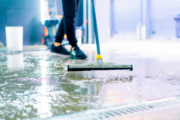 lähikuva autopesulatyöntekijästä poistamassa vettä ja vaahtoa lattiasta autopesulaatikossa, jossa on moppi päivän työn jälkeen - Valokuva, kuva
