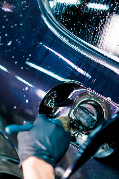 Primer plano de un empleado de lavado de autos lavando el espacio de la tapa de combustible de un automóvil azul de lujo usando un cepillo - Foto, Imagen