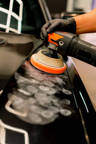 Gros plan d'un employé de lavage de voiture utilisant une polisseuse pour polir le capot d'une voiture de luxe noire - Photo, image