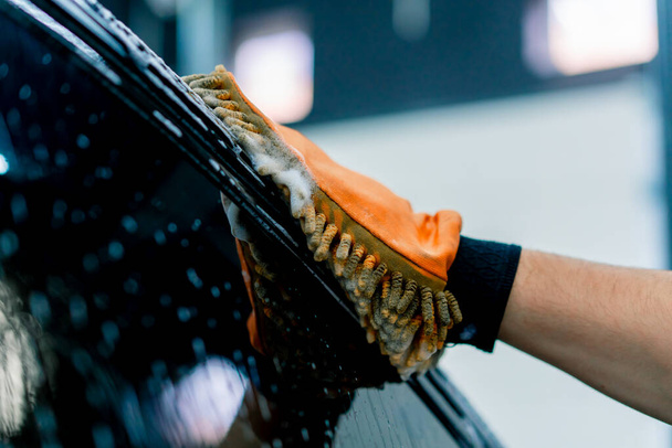 洗車シャンプー付きブラックラグジュアリーカーを洗浄するマイクロファイバー布を使用した洗車作業員のクローズアップ - 写真・画像