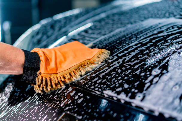 Lähikuva autopesulatyöntekijä käyttää mikrokuituliina pestä musta ylellinen auto pesu shampoo - Valokuva, kuva