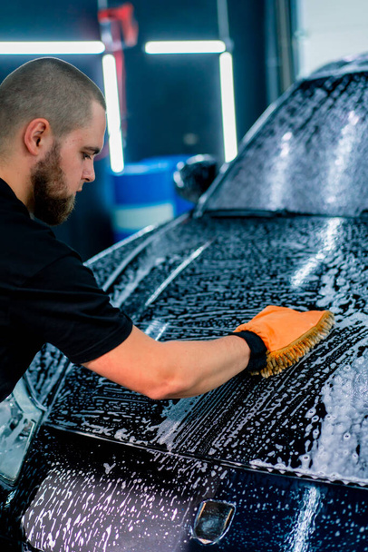 Gros plan d'un ouvrier de lavage de voiture utilisant un chiffon en microfibre pour laver une voiture de luxe noire avec un shampooing de lavage de voiture - Photo, image
