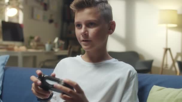Közepes lövés tini fiú ül a kanapén otthon, és játszik konzol videojáték - Felvétel, videó