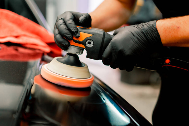 Close-up of a car wash worker using a polishing machine to polish the hood of  black luxury car - Fotografie, Obrázek