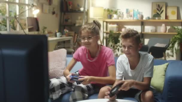 Vrolijke tiener broer en zus zitten op de bank thuis en spelen samen videospel op tv - Video