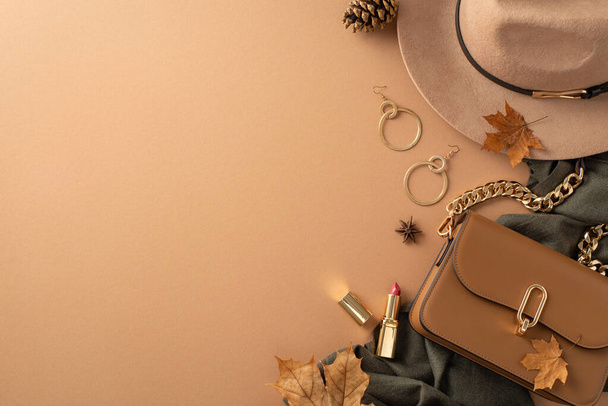 Classic female attire with autumnal touch. Top view of brimmed hat, grey scarf, handbag, gold earrings, lip color, scattered leaves, anise, pine cone on beige backdrop with blank area for text or ad - Photo, Image