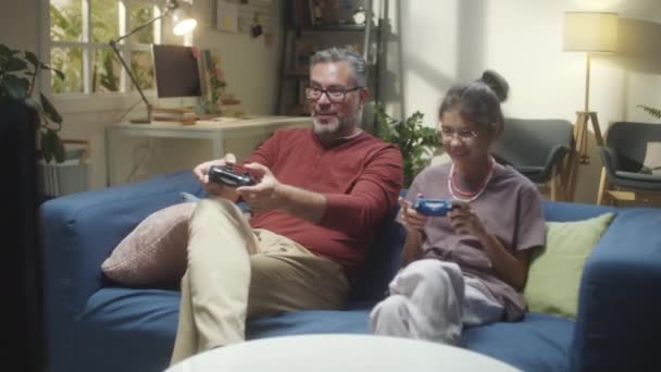 Heyecanlı orta yaşlı baba ve genç kız evde video oyunu oynarken eğleniyorlar. - Video, Çekim