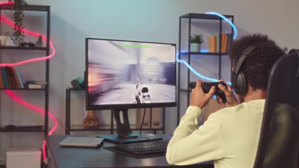 Знімок заднього виду хлопчика-підлітка з використанням контролера під час гри в fps онлайн на ПК вдома - Кадри, відео