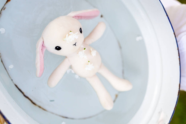 Brinquedos infantis, cuidado com brinquedos, infância. Um coelho de brinquedo branco com orelhas cor de rosa em uma bacia de metal com água no jardim - Foto, Imagem