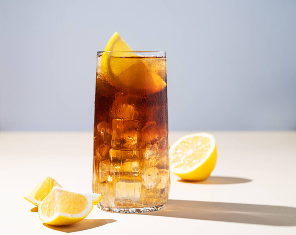 Iced tea with lemon and ice in a tall glass on a yellow background. The concept of a refreshing drink or lemonade on a hot summer day. Front view and copy space. - Valokuva, kuva