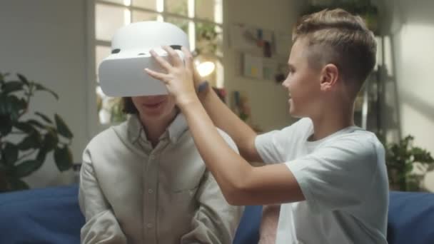 Teenager hilft Mutter beim Anlegen eines VR-Headsets für das Spielen in Augmented Reality zu Hause - Filmmaterial, Video