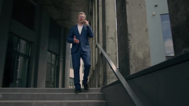 Kaukázusi érett idős férfi üzletember idősebb üzleti munkáltató séta szabadban a lépcsőn közelében irodaépület beszélő telefon ellenőrzés ideje nézi csukló óra késő rohanás siet aggódó futás késés - Felvétel, videó