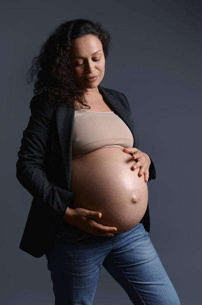 Güzel hamile bir kadının portresi çıplak karnını gerilme izleriyle okşuyor, izole gri stüdyo arka planı. 40 haftalık. 9 aylık tasasız hamileliğin kutlu olsun. Doğumhane. Vücut pozitifliği - Fotoğraf, Görsel