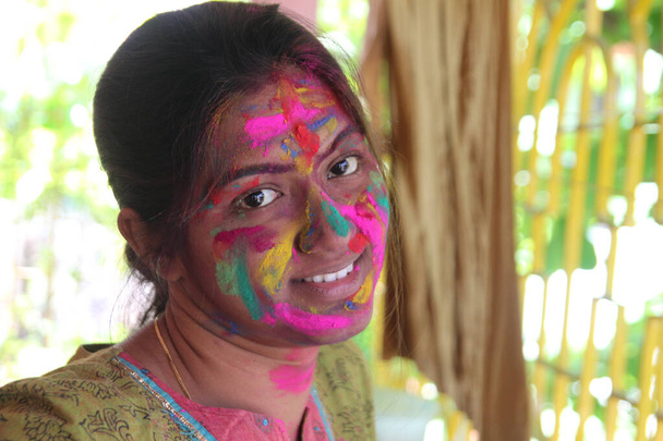 Una mujer india de 30 años con la cara llena de colores vibrantes y mirando hacia la cámara y sonriendo-Holi concepto de imagen - Foto, Imagen