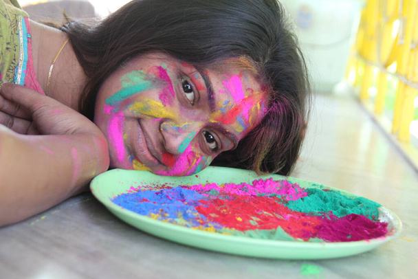 Una mujer india de 30 años con la cara llena de colores vibrantes y mirando hacia la cámara y sonriendo-Holi concepto de imagen - Foto, Imagen