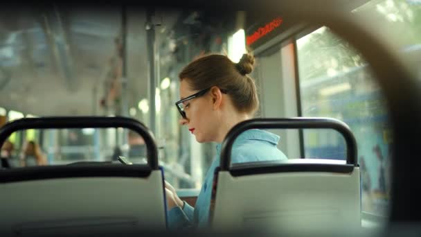 Transports publics. Femme en lunettes dans le tramway en utilisant smartphone bavardage et textos avec des amis, vue arrière, ralenti. Ville, ville, transport. - Séquence, vidéo
