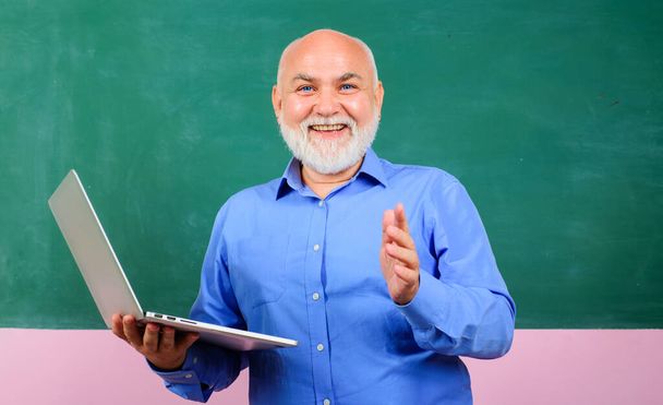 Uśmiechnięty nauczyciel z laptopem przed tablicą w klasie. Nauczyciel daje lekcje uczniom. E-learning na uniwersytecie. mężczyzna nauczyciel z notebooka pracy w biurze prezentując szkolenia biznesowe - Zdjęcie, obraz
