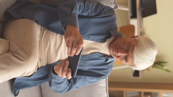 Вертикальный кадр белого взрослого седого мужчины, играющего в игру на смартфоне дома - Кадры, видео