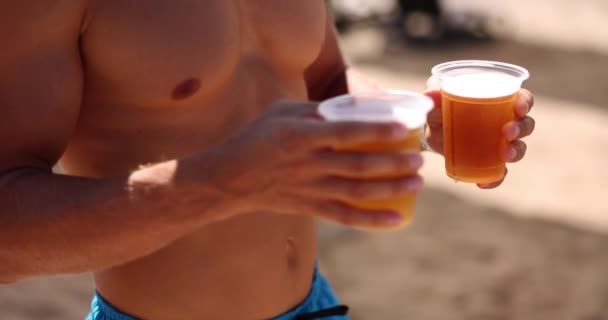 Op het strand houdt een jongeman bier in zijn handen, een close-up, slow motion. Zee vakantie, concept open grens - Video