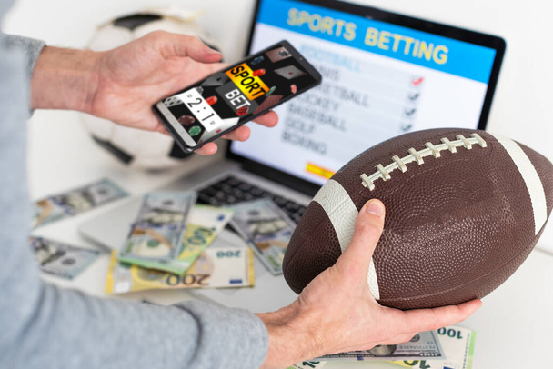 Man betting on sports using smartphone and laptop at table, closeup. Bookmaker websites on displays. High quality photo - Photo, Image