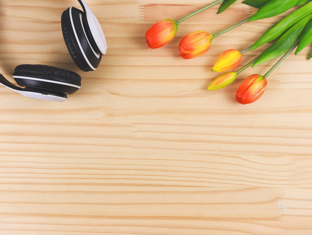 Vista superior de auriculares blancos y flores de tulipán amarillo rojo sobre fondo de mesa de madera con espacio para copiar. Canción de amor, música de primavera, podcast y audiolibro. - Foto, Imagen