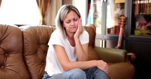 Žena sedící doma na gauči si hladí obličej, zblízka, zpomaleně. Bolest v čelisti, bolest zubů - Záběry, video