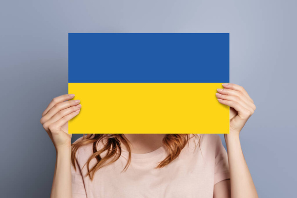 女性は灰色のスタジオの背景の上に隔離されたウクライナの旗と空白のスピーチバブルを保持します - 写真・画像