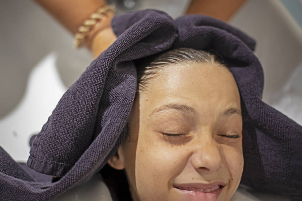 menino adolescente feliz fica com a cabeça esfregada com uma toalha antes de começar um corte de cabelo. salão de beleza - Foto, Imagem